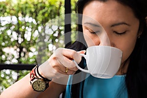 Happy beautiful young woman drinking a cup of hot espresso coffee at the coffee shop as breakfast in the morning. Caucasian female