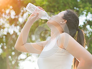 Happy beautiful young woman drinking water from bottle with tree leave background.