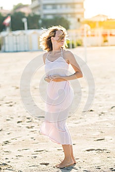 Happy beautiful young woman enjoying sun and wind at the sand beach