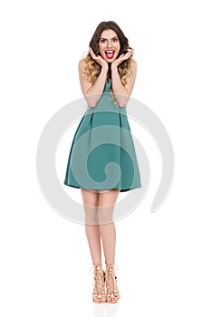 Happy Beautiful Young Woman In Green Mini Dress And High Heels Is Holding Head In Hands And Shouting