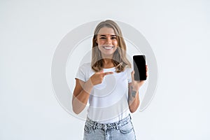 Happy beautiful young woman holding blank screen mobile phone and pointing finger over white background