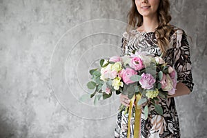 Happy beautiful young woman holding bouquet of mixed flowers standing near the wall. selective focus