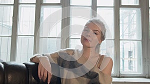 Happy beautiful young woman laughing while looking at the camera. A blonde is smiling at home against the window.