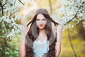 Happy beautiful young woman with long black healthy hair enjoy fresh flowers and sun light in blossom park at sunset.