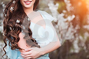 Happy beautiful young woman with long black healthy hair enjoy fresh flowers and sun light in blossom park at sunset.