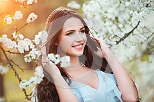 Happy beautiful young woman with long black healthy hair enjoy fresh flowers and sun light in blossom park at sunset.