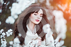 Happy beautiful young woman with long black healthy hair enjoy fresh flowers and sun light in blossom park at sunset.