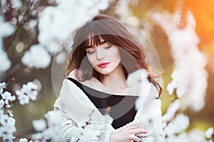 Happy beautiful young woman with long black healthy hair enjoy fresh flowers and sun light in blossom park at sunset.