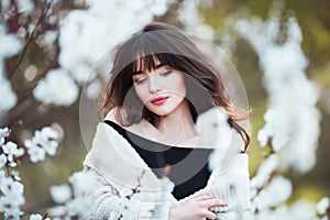 Happy beautiful young woman with long black healthy hair enjoy fresh flowers and sun light in blossom park at sunset.