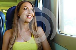 Happy beautiful young woman looking through the train or bus window. Smiling pretty train passenger traveling sitting in a seat