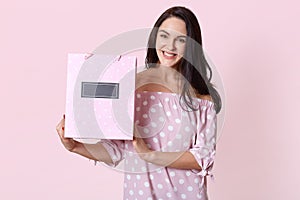 Happy beautiful young woman in polka dot dress, holding shopping bags in her hands and smiling happily. Studio shot of happy