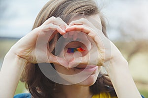 Happy beautiful young woman with rainbow lgbtq eyelashes making heart sign with her hands