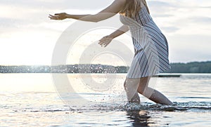 Happy beautiful young woman splashing water in lake with hands.