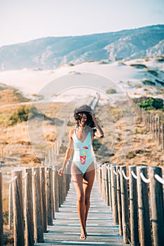 Happy beautiful young woman with a swimming suit running in a wooden foot bridge at the beach
