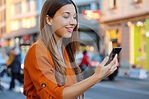 Happy beautiful young woman using smart phone outdoor with blurred background of city street, selective focus. City lifestyle