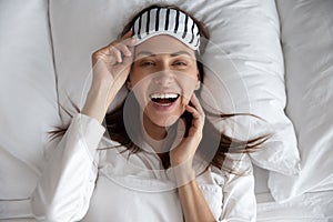 Happy beautiful young woman wear sleeping mask lying in bed