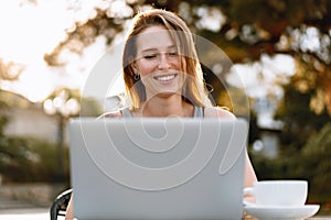 Happy beautiful young woman working on laptop in street cafe