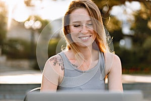 Happy beautiful young woman working on laptop in street cafe