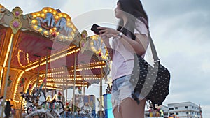 Happy beauty asian woman look at smart phone and seeking friend in amusement park background with carousel ride background. People