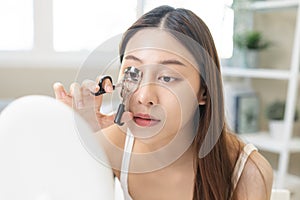 Happy beauty concept, asian young woman, girl make up face hand using eyelash curler on long eyelash before applying mascara brush