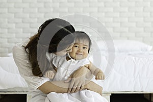 Happy Beauty mother Holding and kissing Cute Sweet Adorable Asian Baby wearing white dress sitting on Carpet