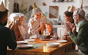 Happy big family in party hats clapping hands while celebrating little boys birthday at home