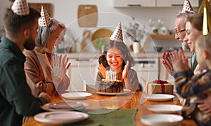 Happy big family in party hats clapping hands while celebrating little girls birthday at home