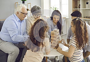 Happy big family plays Jenga at home and takes turns taking bricks out of a wooden tower.