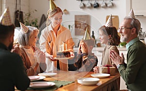 Happy big family surprising excited little boy by bringing Birthday chocolate cake with lit candles