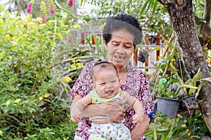 Happy big laughing child boy and senior woman holding adorable baby boy in flowery garden