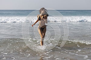 Happy bikini beach vacation woman running to ocean splashing water in freedom feeling. Happiness carefree lifestyle