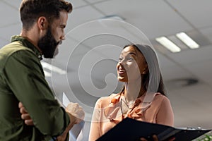 Happy biracial businesswoman discussing over document with caucasian businessman in workplace