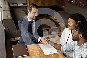 Happy biracial couple handshake male realtor at meeting