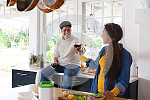 Happy biracial couple preparing food and drinking red wine in kitchen