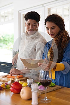 Happy biracial couple preparing food using recipe on tablet in kitchen