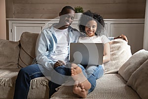 Happy biracial couple relax on couch using laptop