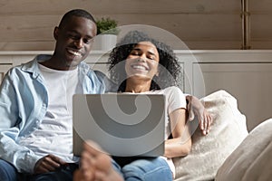 Happy biracial couple relax laugh using laptop at home