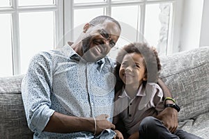 Happy biracial dad and son cuddle on couch