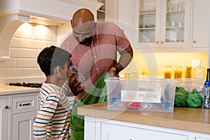 Happy biracial father and son bagging rubbish for recycling in kitchen