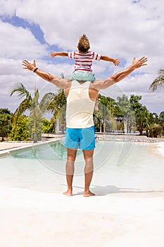 Happy biracial father and son widening arms by the swimming pool