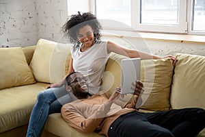 Happy african American couple relax on sofa using tablet