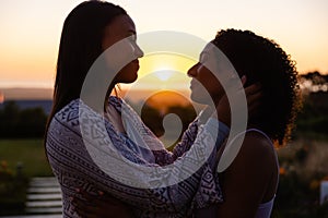 Happy biracial lesbian couple embracing in garden at sunset