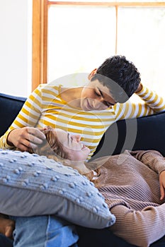 Happy biracial lesbian couple relaxing on couch together talking at home, copy space