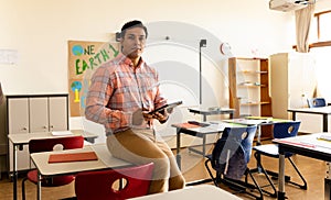 Happy biracial male teacher with tablet in elementary school classroom