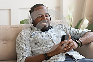 Happy biracial man listen to music resting on couch