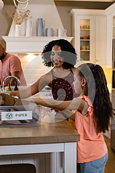 Happy biracial parents and daughter sorting rubbish for recycling on kitchen counter, copy space