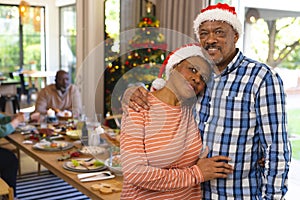 Happy biracial senior couple embracing and smiling at christmas meal with friends