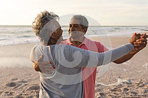 Happy biracial senior man enjoying romantic dance with woman at beach during sunset