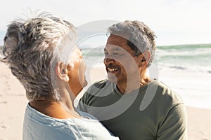 Happy biracial senior man and woman looking at each other while smiling on sunny beach