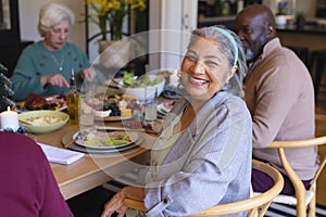 Happy biracial senior woman celebrating with friends at christmas dinner in sunny dining room